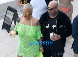 January 18, 2015: Amber Rose removes her neon green mesh cover-up to reveal a sheer yellow bikini top by the pool in Miami.