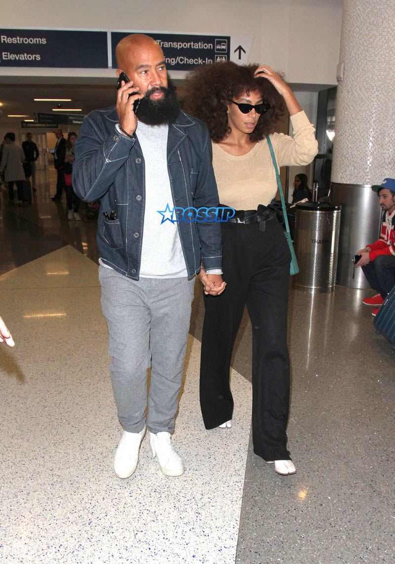 Solange Knowles husband, Alan Ferguson at LAX with highwater pants, camel-toe shoes and a beige top. SplashNews beard denim jacket white sneakers holding hands