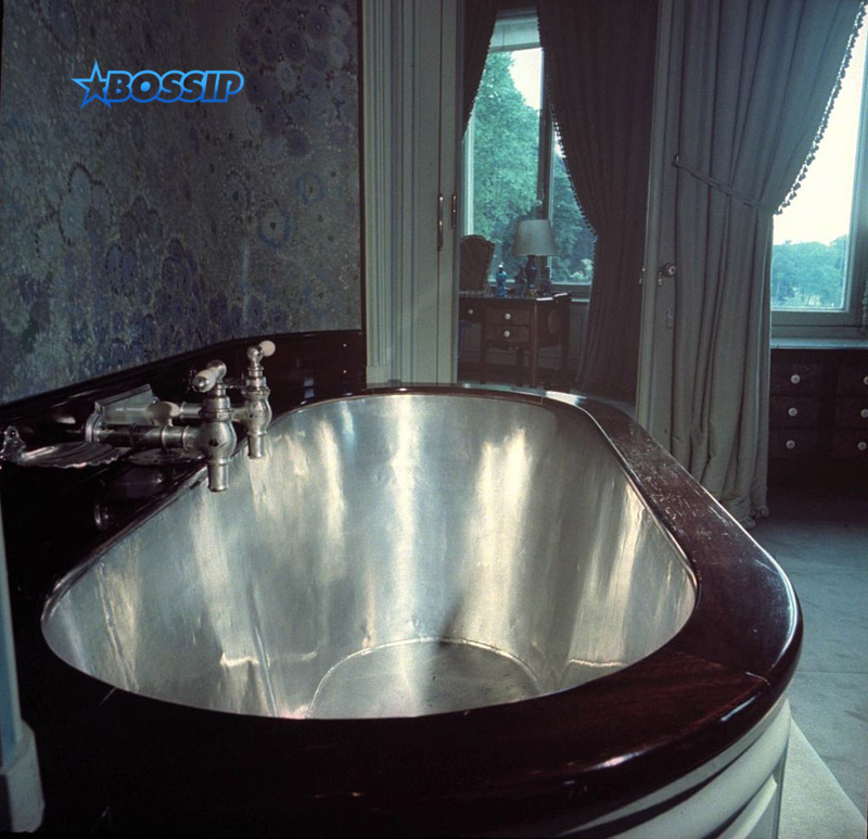 Interior of a bathroom with a silver bathtub set in mahogany, blue wallpaper and a window looking out in the garden of Ferrieres, the Rothschild country home.