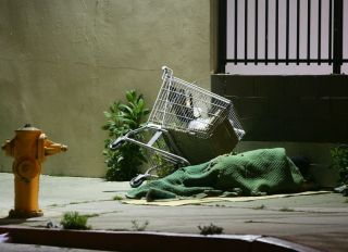 LOS ANGELES, CA - APRIL 19: A homeless person sleeps by his shopping cart on a downtown sidewalk in the early morning hours of April 19, 2006 in Los Angeles, California. Most homeless tents and improvised shelters are taken down at dawn, before their possessions can be hauled away by cleaning crews. A 9th U.S. Circuit Court of Appeals panel ruled last week that a city law making it illegal to sleep or sit on city sidewalks cannot be implemented as long as there is a shortage of homeless shelter beds in Los Angeles. According to a study released in January by the Los Angeles Housing Services Authority, there are nearly 90,000 homeless people live in Los Angeles County but only 9,000 to 10,000 beds available in homeless shelters, single-room occupancy hotels, and other facilities