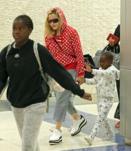 Madonna rocks a red supreme louis vuitton hoodie while touching down at JFK airport in New York holding her twins hands Estere and Stelle while Lourdes, David, and Mercy in tow after celebrating her 59th birthday in Italy.
