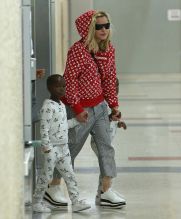 Madonna rocks a red supreme louis vuitton hoodie while touching down at JFK airport in New York holding her twins hands Estere and Stelle while Lourdes, David, and Mercy in tow after celebrating her 59th birthday in Italy.