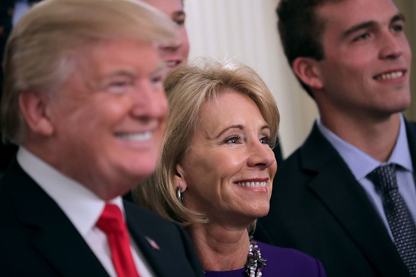 WASHINGTON, DC - NOVEMBER 17:  (AFP OUT) U.S. President Donald Trump and Education Secretary Betsy Devos pose for photographs with members of the National Collegiate Athletic Association's champion University of Virginia men's tennis team in the East Room of the White House November 17, 2017 in Washington, DC. The White House welcomed athletes representing universities and colleges from across the country to meet Trump who congratulated them on their NCAA victories in sports like lacrosse, bowling, gymnastics, golf, rowing and others. 