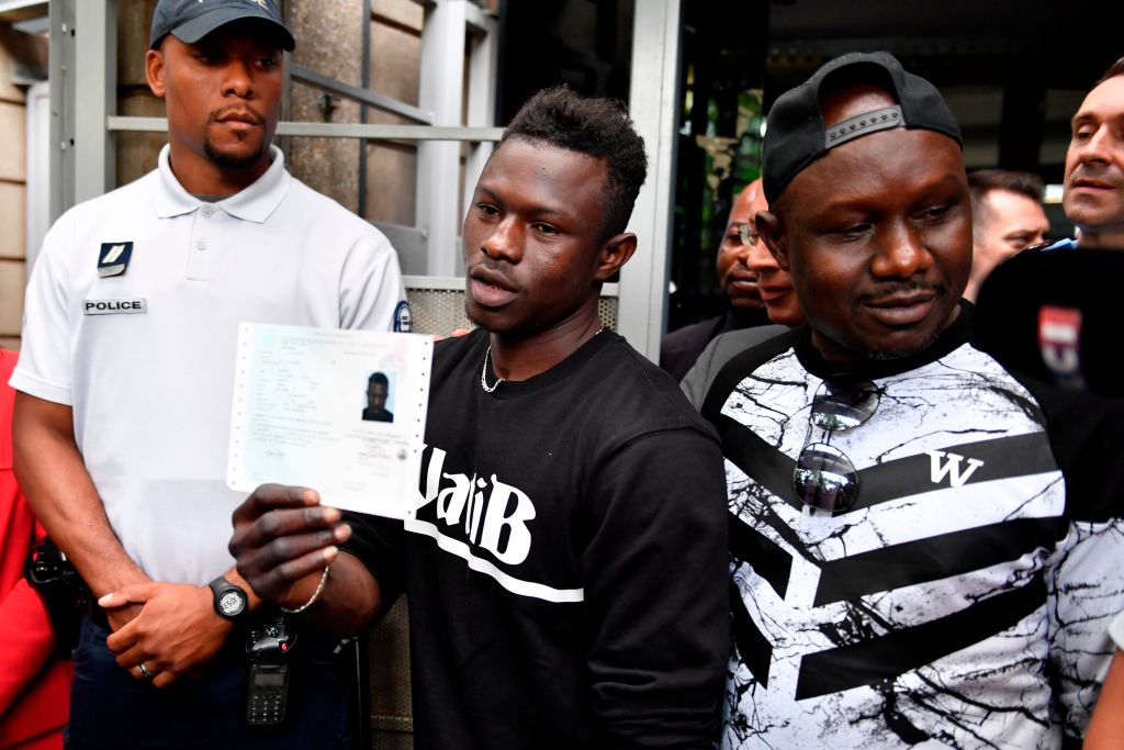 Malian migrant Mamoudou Gassama (C) flanked by his older brother (R) holds his temporary residence permit after receiving it at the Prefecture of Bobigny, northeast of Paris on May 29, 2018, one day after he was honored by the French President for scaling an apartment building to save a 4-year-old child dangling from a fourth-floor balcony. - Two days after his daring rescue -- viewed millions of times online -- Mamoudou Gassama, 22-year old,  nicknamed 