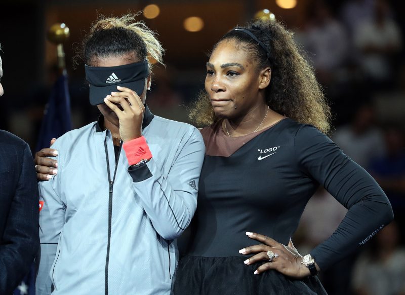 Tennis players Naomi Osaka hides her face and cries while standing next to Serena Williams during the trophy presentation ceremony for the Single Women's Title at the 2018 U.S. Open in New York, NY. Serena Williams would then comfort her and the two would get their trophies.