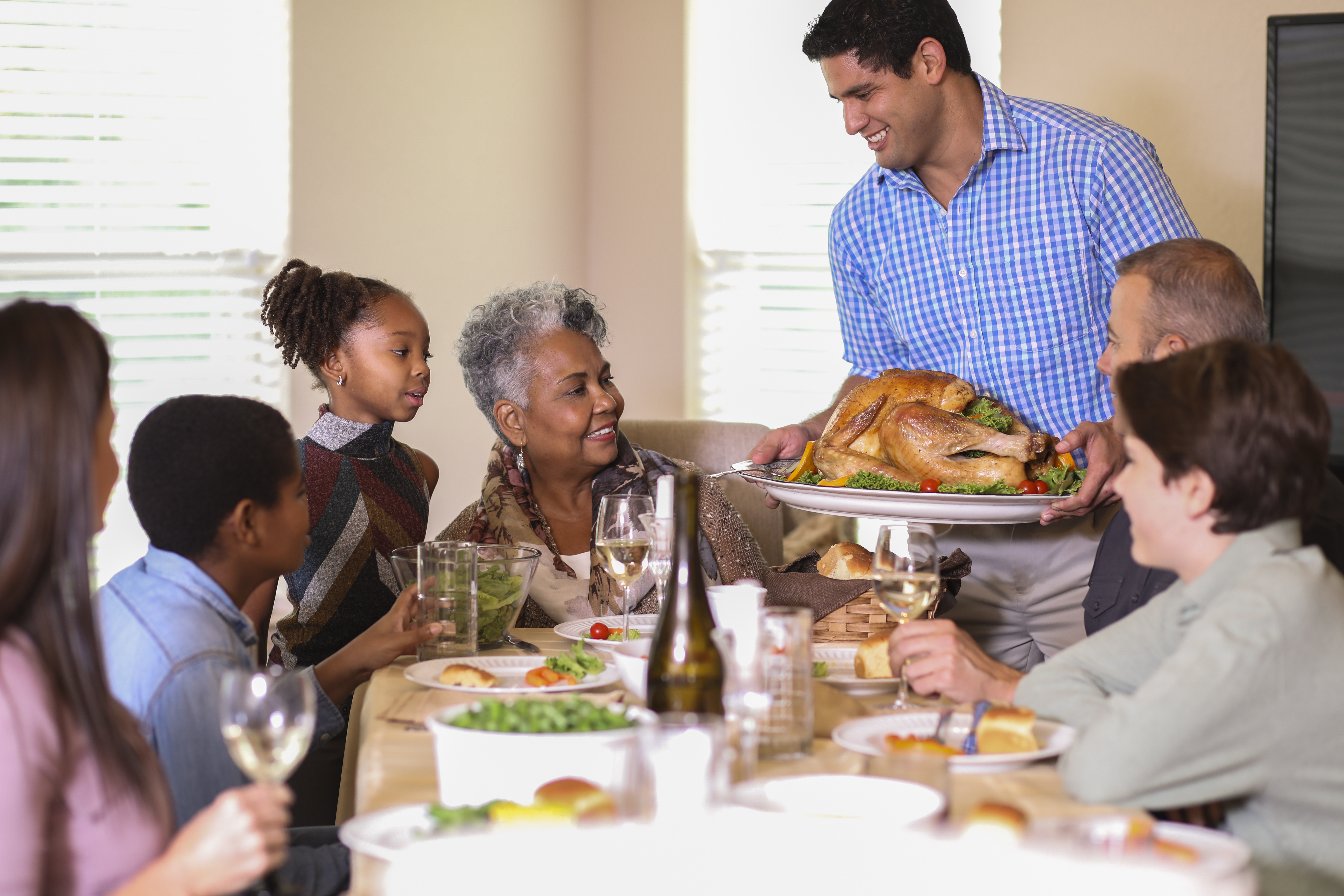Diverse family at dining table eating Thanksgiving dinner.