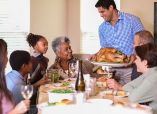 Diverse family at dining table eating Thanksgiving dinner.