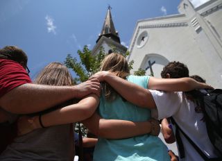 CHARLESTON, SC - JULY 17: A church youth group from Douthan, Alabama prays in front of the Emanuel AME Church on the one-month anniversary of the mass shooting on July 17, 2015 in Charleston, South Carolina. Visitors from around the nation continue to pay their respects at a makeshift shrine in front of the church, in a show of faith and solidarity with "Mother Emanuel", as the church is known in Charleston. Nine people were allegedly murdered on June 17 by 21-year-old white supremacist Dylann Roof, who was captured by police in North Carolina the following day. He is scheduled to go to trial July 11, 2016.