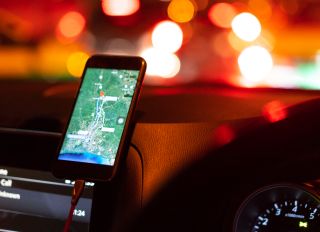 The map on the phone in the background of the dashboard. Black mobile phone with map gps navigation fixed in the mounting. App map for travel.