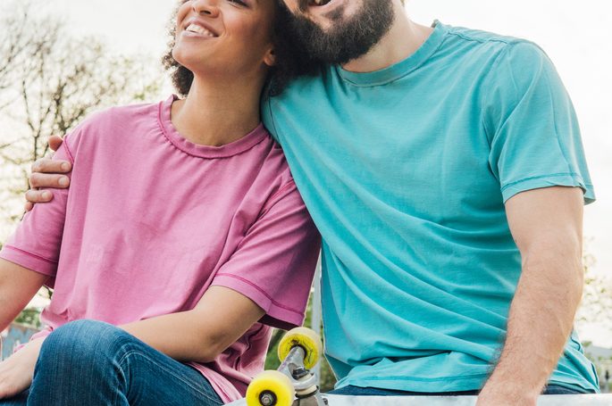 Smiling skater man hugging his girlfriend while sitting in the park