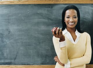 Portrait of a Teacher Standing in Front of a Blackboard Eating an Apple