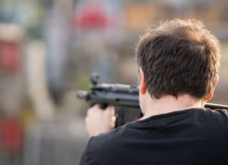 Rear View Of Man Shooting Gun Outdoors
