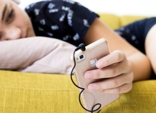 Girl lying on the couch at home listening music with headphones and smartphone