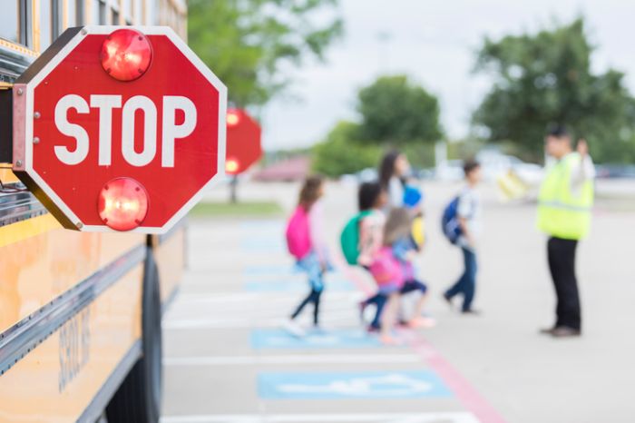 Lights flash on a school bus stop sign as children cross street