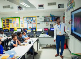 Male teacher leading lesson at touch screen in classroom