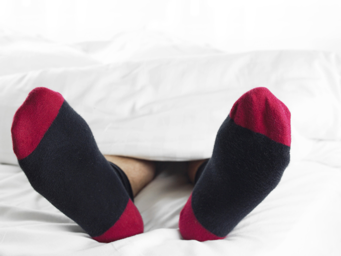 Man Wearing Socks Underneath a Duvet in Bed
