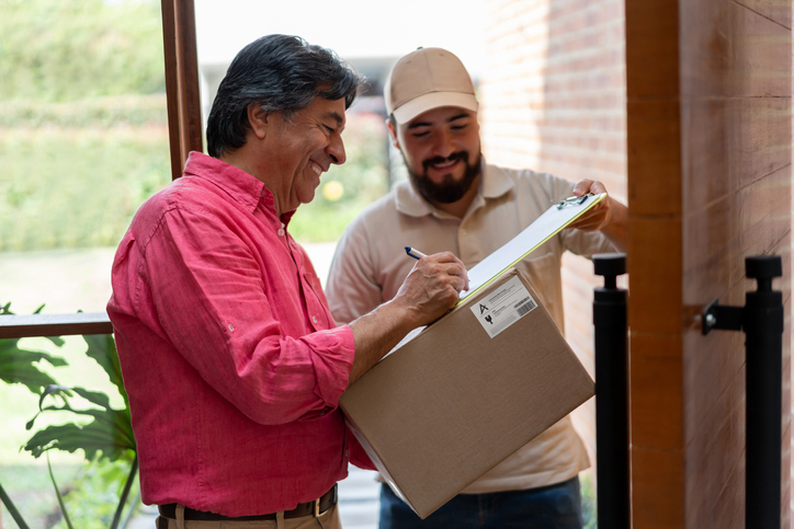 Senior man at home receiving a package and signing a document while postal worker holds clipboard