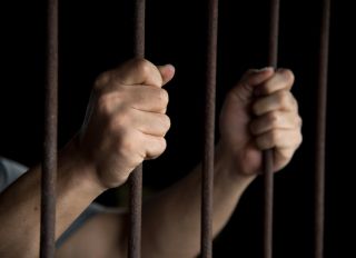 Close-Up Of Man Holding Prison Bars