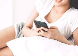 Midsection Of Young Woman Using Mobile Phone While Lying On Bed At Home