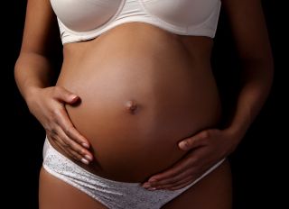 Midsection Of Pregnant Woman Touching Abdomen While Standing Against Black Background
