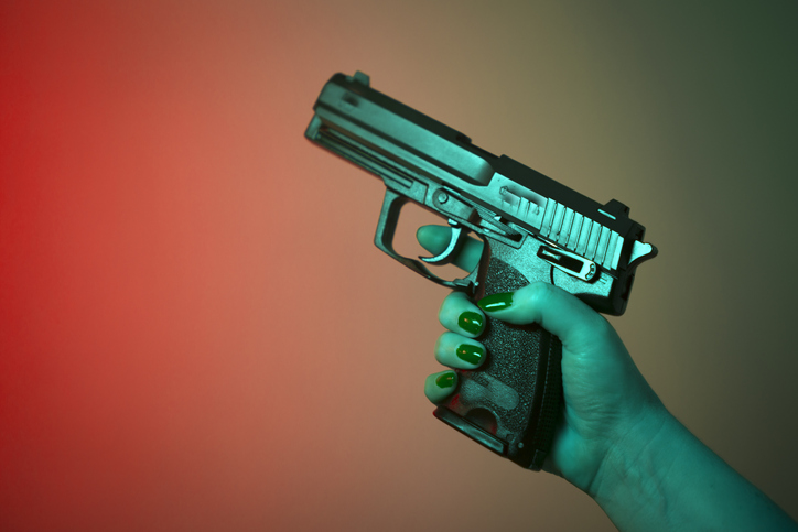 Cropped Hand Of Woman Holding Handgun Against Colored Background