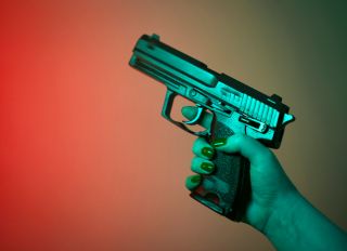 Cropped Hand Of Woman Holding Handgun Against Colored Background