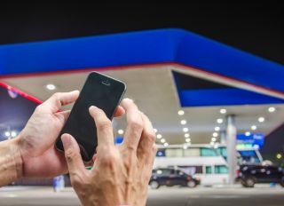 Cropped Hand Of Person Using Mobile Phone Against Gas Station At Night