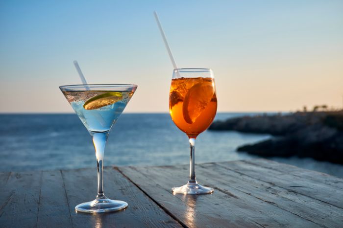 Glass of ice-cooled Spritz with orange slice and glass of Martini with lime slice in front of the sea