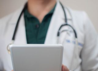 A young doctor in white coat is using a digital tablet