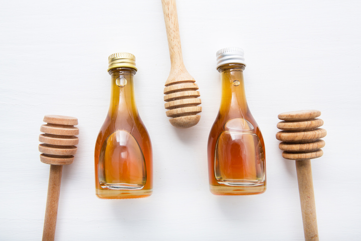 Directly Above Shot Of Honey In Bottles With Dippers Over White Background