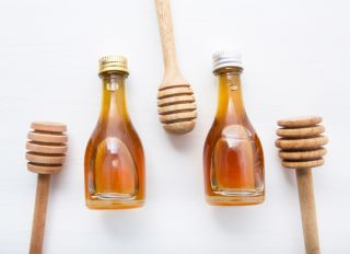 Directly Above Shot Of Honey In Bottles With Dippers Over White Background