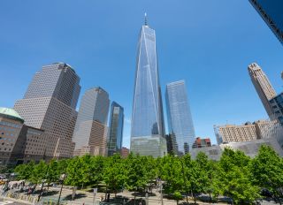 Fresh green trees grow and surround the 9/11 Memorial in spring at Lower Manhattan New York. One World Trade Center and the other lower Manhattan skyscrapers stand behind the 9/11 Memorial.