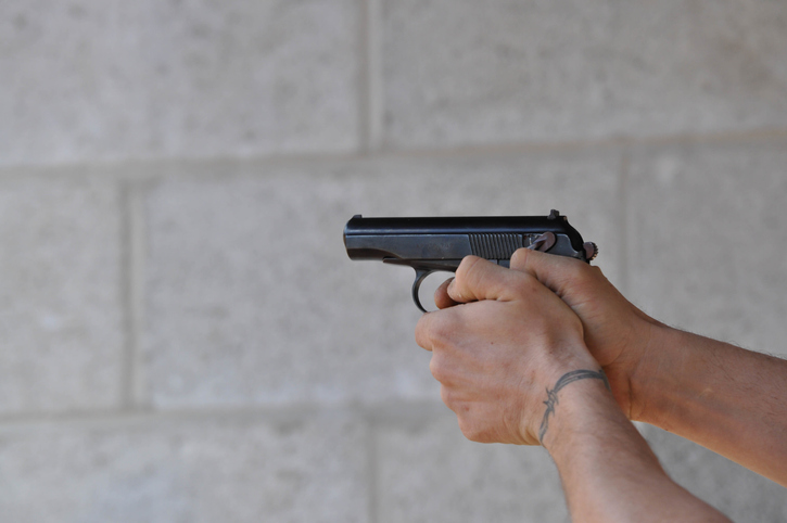 Close-Up Of Man Holding Gun Against Wall