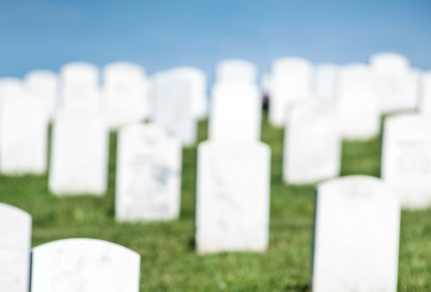 Blank white veteran burial tombstone with rows of headstones in background in military cemetery