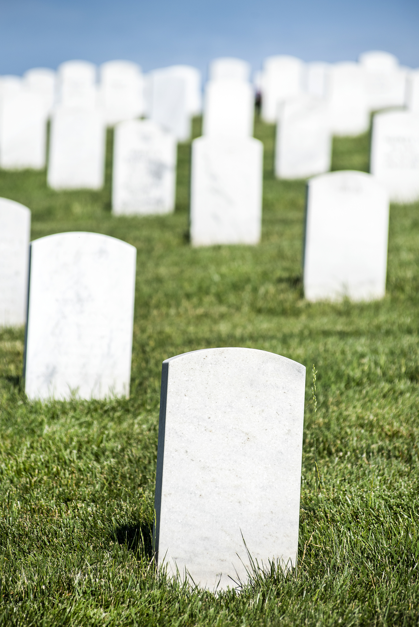 Blank white veteran burial tombstone with rows of headstones in background in military cemetery