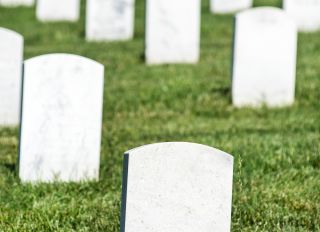 Blank white veteran burial tombstone with rows of headstones in background in military cemetery