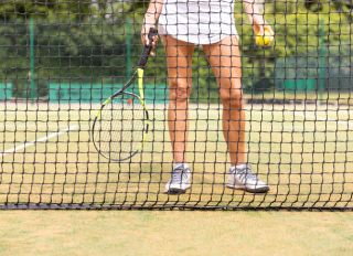Female tennis player legs on grass court seen through the net