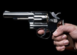 Cropped Hand Of Man Holding Gun Against Black Background