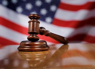 Close-Up Of Gavel On Wooden Table Against American Flag