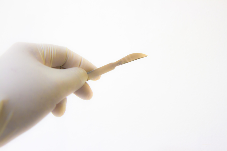 Close-Up Of Hand Holding Scalpel Over White Background