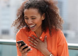Laughing Black woman text messaging on cell phone - stock photo