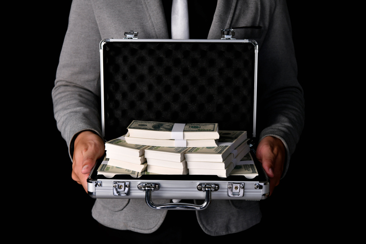 Midsection Of Businessman Holding Briefcase With Paper Currencies Against Black Background