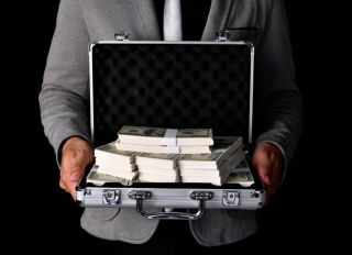 Midsection Of Businessman Holding Briefcase With Paper Currencies Against Black Background