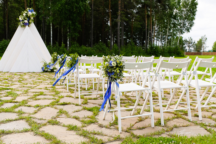 White wooden chairs decorated with flowers and bright satin ribbons, wedding decor at the ceremony in the pine forest