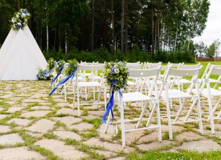 White wooden chairs decorated with flowers and bright satin ribbons, wedding decor at the ceremony in the pine forest