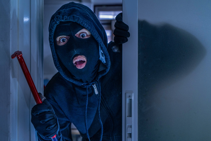 masked burglar with crowbar breaking and entering into a victim's home