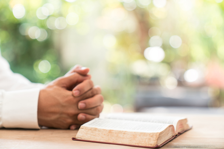 Close-Up Of Hands Clasped By Book On Table