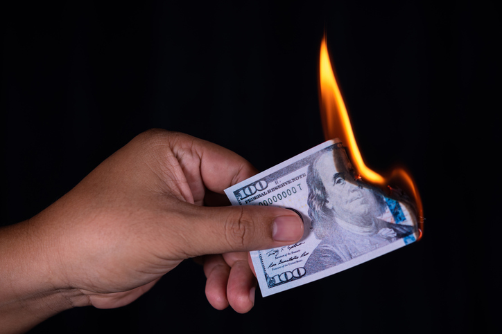 Close-Up Of Hand Holding Burning Paper Currency Against Black Background