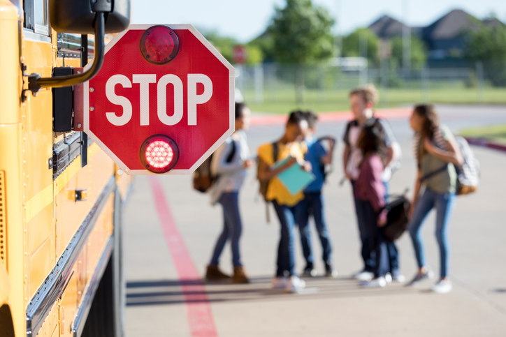 Group of school children talk outside bus