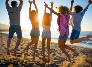 Group of friends jumping for joy on the beach at sunset or sunrise.